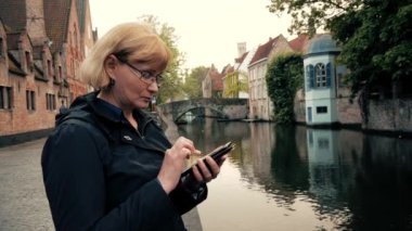 İşkadını siyah montlu nehir kanalı oturan telefon App kullanır