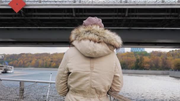 View Back Woman In Beige Jacket With Fur On Ship Floats Down River Under Bridge — Stock Video