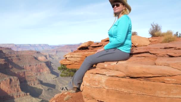 Turistické žena sedící na skále houpající se jí nohy a obdivuje názory Grand Canyon — Stock video