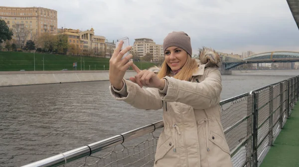 Kvinna Selfie på Smartphone stående på banvallen av floden och utsikt över staden Stockbild