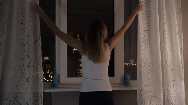 Жінка стенди на вікна вночі, дивлячись на вуличних ліхтарів, штори Ліцензійні Стокові Фото
