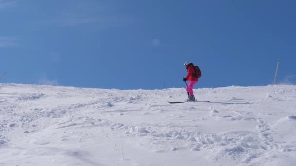 Mujer rueda lentamente por la montaña esquiando en una pendiente empinada con rocas — Vídeos de Stock