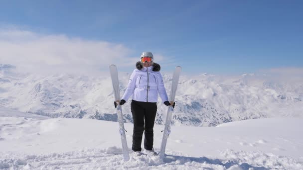 Mujer feliz levanta sus esquís cuesta abajo en la cima de la montaña — Vídeo de stock