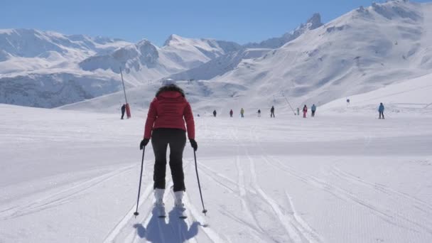 Achteraanzicht van een skiër vrouw duwt de skistokken om te skiën — Stockvideo