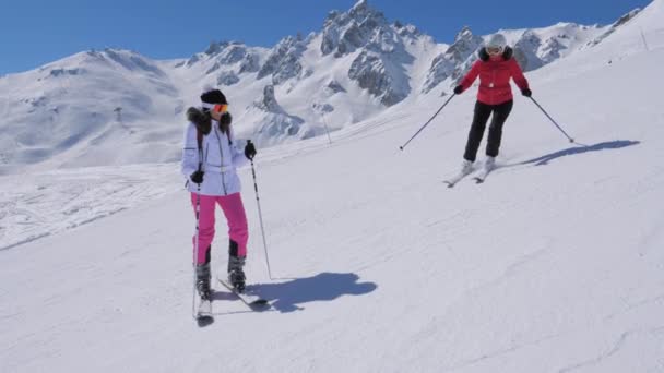 Mujer esquiadora se para en la pista de esquí de montaña, cerca de sus frenos su amiga y saluda — Vídeos de Stock