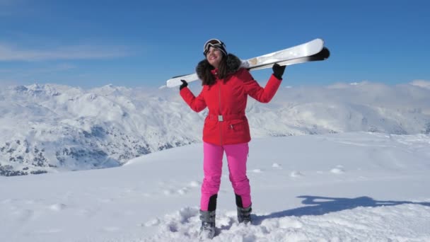 Σκιέρ γυναίκα στέκεται πάνω σε πλαγιά βουνού, κρατώντας τα χέρια του σκι στους ώμους — Αρχείο Βίντεο