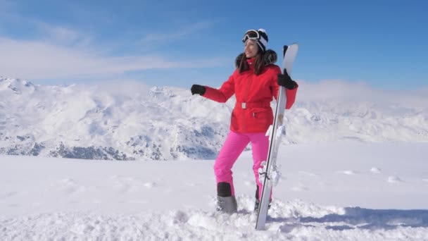 Mujer sosteniendo esquís, usando gafas, de pie fondo montañas cubiertas de nieve — Vídeo de stock