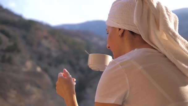 Žena pije šálek čaje nebo kávy v paprscích slunce na terase v horách — Stock video