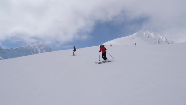 两个滑雪者慢慢地在滑雪板上的天空后, 滑雪胜地的斜坡上 — 图库视频影像