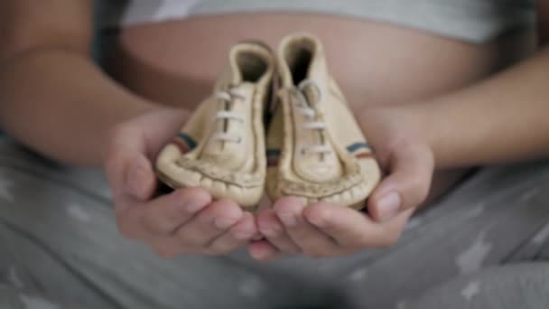 Schwangere zeigt ihren Händen schöne kleine Schuhe für ein Baby aus nächster Nähe — Stockvideo