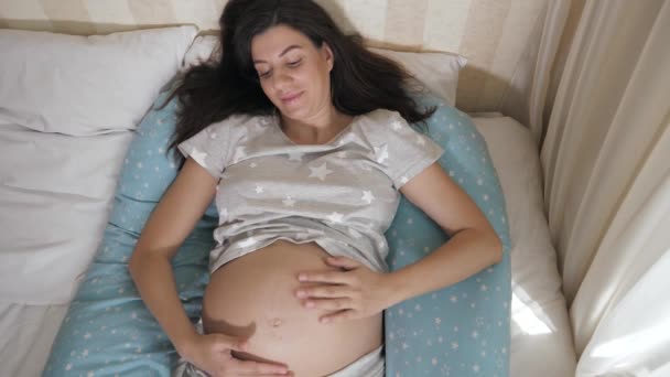 Embarazada mujer acariciando abdomen con su mano mentir en la cama — Vídeo de stock