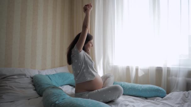 Η έγκυος γυναίκα ξυπνάει τεντώνει τα χέρια της και χαϊδεύει τη μεγάλη της κοιλιά. — Αρχείο Βίντεο