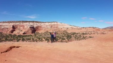 İHA kollarını sallayarak iki turistten uzaklaşıyor ve kayaların üzerinde duruyor.