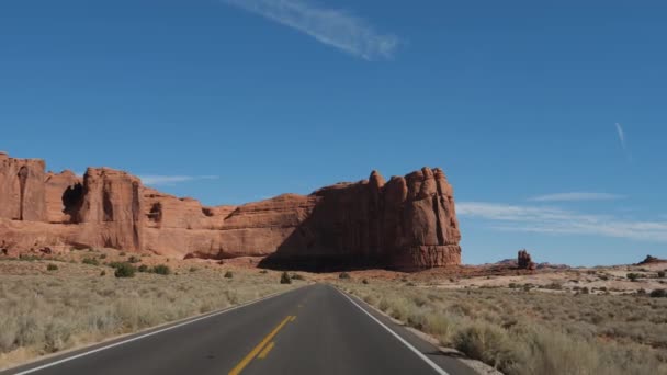 Conduire sur la route vide à travers le parc national des Arches avec des rochers rouges dans le désert États-Unis — Video