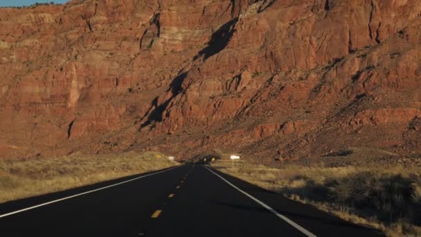 Hajt az úton a sivatagi háttér egy magas fal egy szikla monolit naplementekor — Stock videók