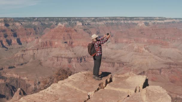 Mulher caminhante tira foto em Smartphone em pé na borda de rochas no Grand Canyon — Vídeo de Stock