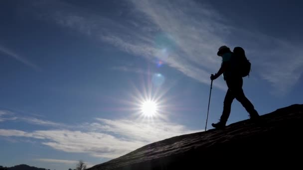Silueta de excursionista activo que baja por la ladera de la montaña contra la puesta de sol — Vídeos de Stock