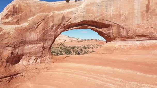 Drone vuela en Red Rock Arch en el que hay dos turistas y las manos ondeantes — Vídeos de Stock