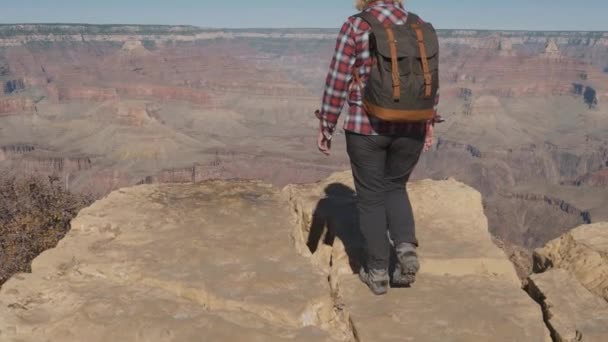 Senderista activa mujer camina al borde de las rocas del Gran Cañón y levanta sus brazos — Vídeos de Stock