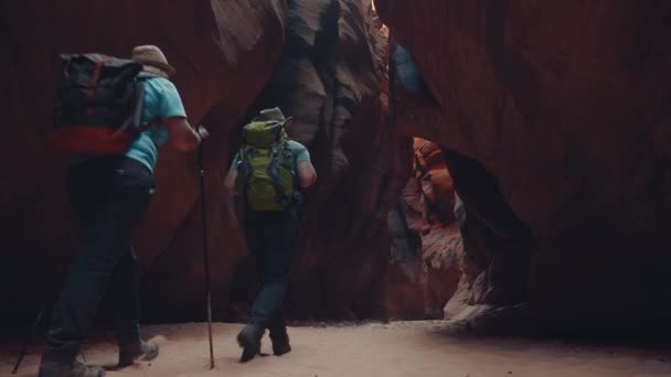 Yürüyüşçüler turuncu kayalarla derin mağara kanyonunda kumlu bir nehir yatağı boyunca yürüyorlar. — Stok video