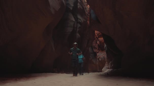 Túrázók túrázás egy homokos folyómeder mély barlang kanyon narancs vörös sziklák — Stock videók