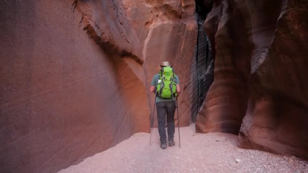 Pěší turistika na suchém korytě řeky v jeskyni hluboké štěrbiny kaňonu s oranžovou křivkou skal — Stock video