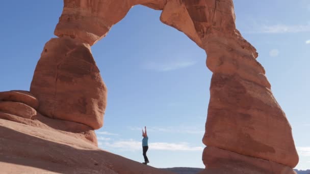 Ο τουρίστας σηκώνει τα χέρια του ψηλά σε μια λεπτή αψίδα του πορτοκαλί βράχου στο εθνικό πάρκο — Αρχείο Βίντεο