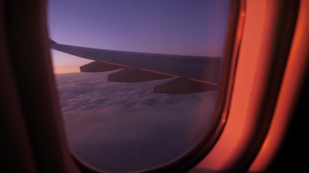 Vista del ala de un avión volando sobre nubes con un cielo al atardecer desde la ventana — Vídeos de Stock