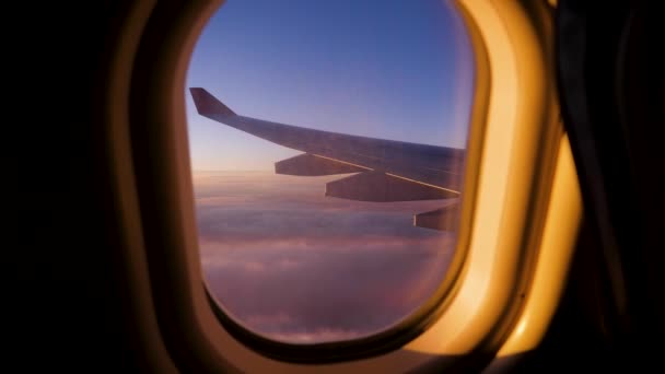 Vista da asa do avião voando sobre nuvens com céu escarlate do por do sol da janela — Vídeo de Stock