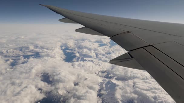 Вид из окна самолета на крыло и горный хребет в снегу и облаках — стоковое видео