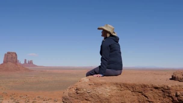 Toerist in cowboy hoed zit op klif van het gezichtspunt in Monument Valley Usa — Stockvideo