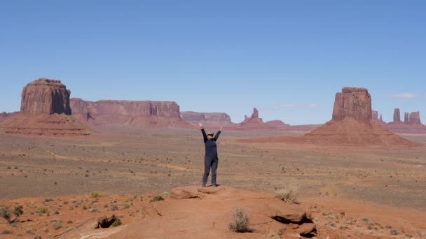 Toerist aan de top en heft haar armen omhoog vieren overwinning in Monument Valley Usa — Stockvideo