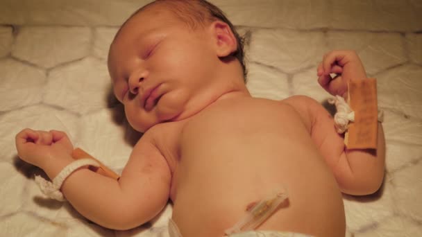 Newborn Is Lying Under Warm Lamp On Changing Table With Name Pendants On His Arm — Stock Video