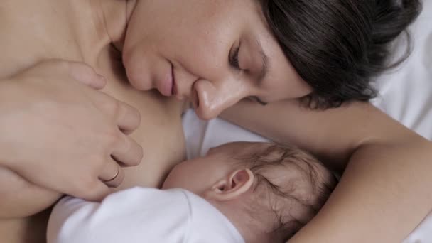 若い女性はベッドで寝そべっている間に彼女の新生児の赤ちゃんに母乳を供給 — ストック動画