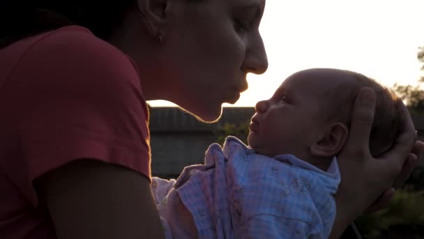 Donna madre tiene il suo neonato tra le braccia e lo bacia contro i raggi del tramonto — Video Stock