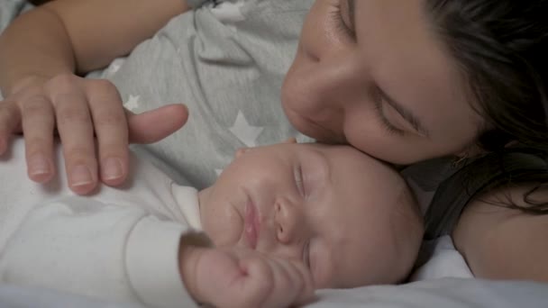 Мать гладит спящего ребенка на животе лежать вместе в постели и целовать его — стоковое видео