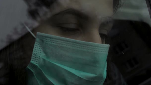 Donna in maschera medica protettiva dietro la finestra di vetro si affaccia sulla strada — Video Stock