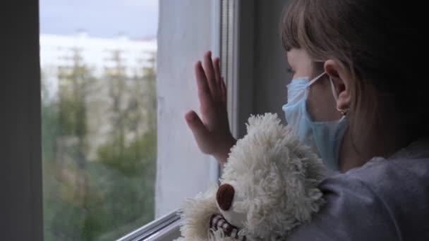 Aranyos lány tartja Teddy Bear néz ki az ablakon az utcán karantén alatt — Stock videók