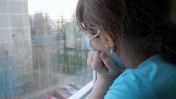 Flicka i skyddande mask med armbågarna på Windowsill ser ut fönstret på gatan — Stockvideo