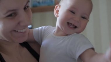 Anne, konuşmaya çalışan neşeli, neşeli bir bebeği kollarında tutuyor.