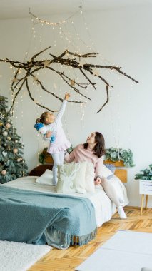 A young beautiful pregnant mom and her little daughter have fun in a stylishly decorated Christmas bedroom. New Year's and Christmas.