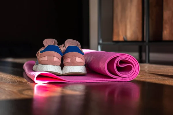 Yoga mat on the wooden floor. One pink yoga man on a brown wooden floor. Sports shoes. Training sneakers. Pink sneakers on yoga mat