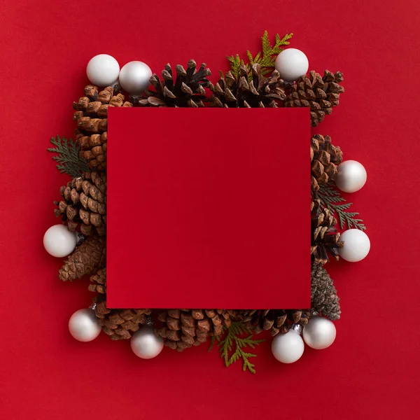 Colocación plana de una tarjeta de felicitación roja vacía en el centro de la composición de protuberancias y bolas blancas sobre el fondo rojo. Concepto de Navidad — Foto de Stock