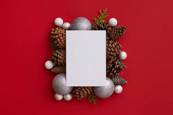 Flat lay of an empty white greeting card in the centre of the composition of bumps and silver and white balls on the red background. Christmas concept — Stock Photo, Image