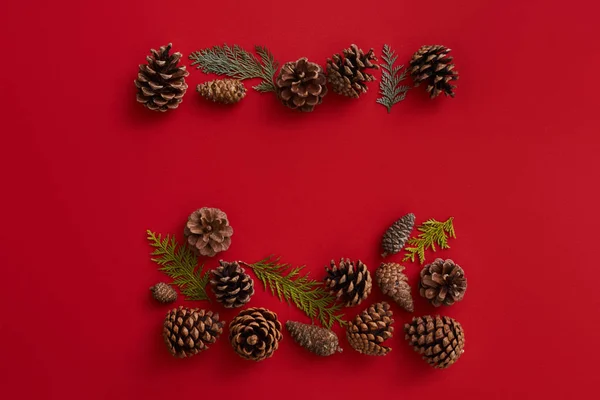 Composição de leigos planos de cones de abeto e ramos de abeto no fundo vermelho. Conceito de Natal — Fotografia de Stock