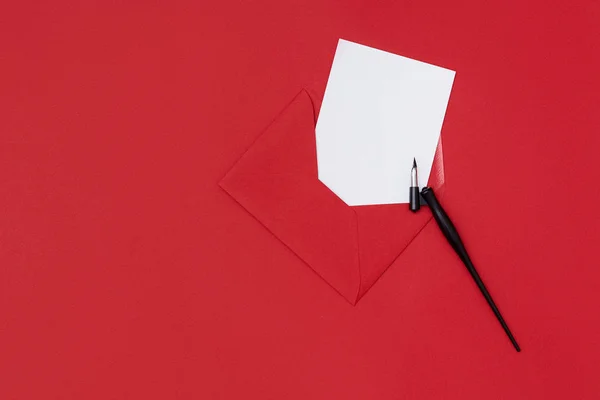 A penholder and an empty mock up postcard in the red envelope on the red background. Valentine's Day concept. Christmas concept — 스톡 사진