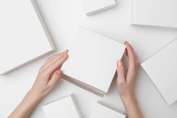 Mock up de caixa de presente branco em mãos de mulheres no fundo branco cercado com muitas caixas brancas de tamanho diferente — Fotografia de Stock