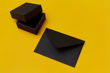 Siyah kağıt hediye kutusu ve sarı arka planda bir zarf. Sunum şablonu