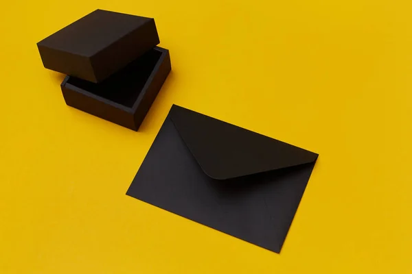 Vysmívejte se černé papírové dárkové krabici a obálce na žlutém pozadí. Šablona prezentace — Stock fotografie