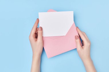 Pink envelope with blank white postcard in womans hands on the blue background. Mail concept clipart